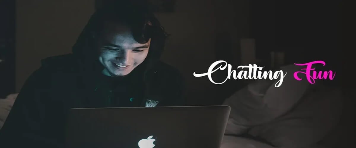 Man sitting in a dark room with a hoodie on and smiling while chatting